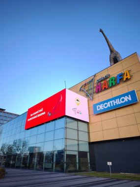 Prag, Çek Cumhuriyeti - 9 Ocak 2025: Çatıya tünemiş bir dinozor heykelinin yer aldığı modern alışveriş merkezi, canlı mavi gökyüzü harfa galerisi alışveriş merkezi Premium OOH 3D reklam panosu