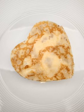 Kalp şeklinde krepler, beyaz seramik tabağı süsleyen krep, Anneler Günü için tatlı aşçılık sunumuyla romantik sabah yemeğini sembolize ediyor.