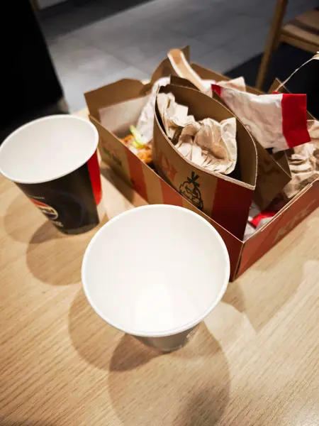 Prag, Çek Cumhuriyeti - 19 Ocak 2025: KFC Kırışık Kağıt ve arta kalan fast food karton bir konteynırda iki boş kağıt bardağın yanında oturmuş,