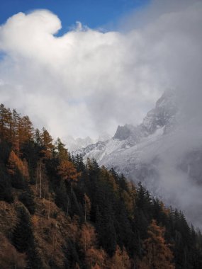 Chamonix yakınlarındaki panoramik dağ manzarası, karlı zirveler, altın sonbahar ağaçları, sonbahar sezonu boyunca dramatik bulutlu arka plan