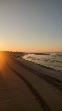 Güneşin doğuşu, bibiyonun kumlu kıyılarını boyar, İtalya, altın ışıkla, plajda kalan lastik izlerini aydınlatır
