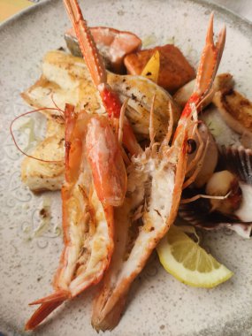 Karides, balık ve limon dilimlerinin yer aldığı dekoratif bir tabakta servis edilen taze ızgara deniz ürünleri, İtalyan mutfağının özünü yansıtıyor.