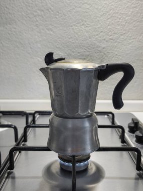 Antika moka demliği, rustik gaz sobasında koyu kahve demliyor, geleneksel mutfak ortamında otantik İtalyan sabah hazırlıklarını yakalıyor.