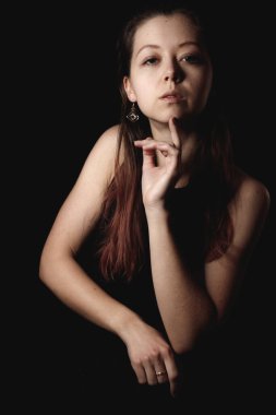 Yüzü koyu renk bir arkaplanda poz veren, küpe ve yüzük takan, iç gözlem ve zarafet kitaplarını taşıyan, koyu arkaplan kaplamalı, düşünceli bir kadın.