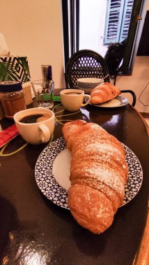 Hırvatistan 'da nefis bir kahvaltı deneyimi için üzerine pudra şekeri serpiştirilmiş taze kruvasanlar kahve fincanlarının yanında servis ediliyor.