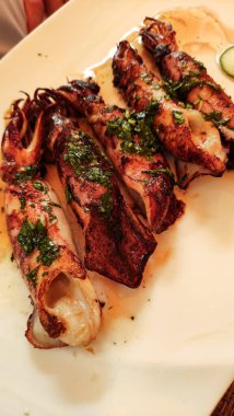 Beyaz bir tabakta servis edilen taze otlarla tatlandırılmış ızgara mürekkep balıkları tipik bir Hırvat yaz yemeğini temsil ediyor.