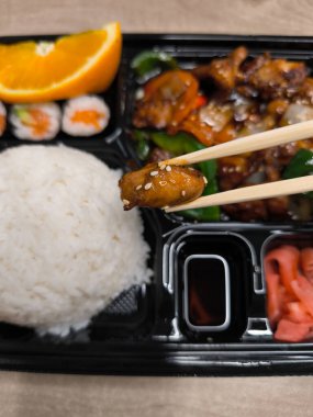 Çubukları kapatın. Bir parça teriyaki tavuğunu pirinç, suşi ve diğer renkli malzemelerle dolu bir bento kutusundan kaldırın.