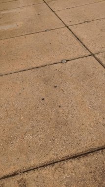 Birbirine kenetlenmiş beton levhalar kaldırımda geometrik desenler oluşturur, aşınma ve yırtılma izleri gösterir.