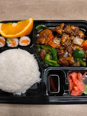 Lezzetli bento kutusu, teriyaki tavuğu, suşi, pirinç ve turşulu zencefil de dahil olmak üzere çeşitli Asya yemekleri sunuyor. Üstüne de portakal dilimli fast food.