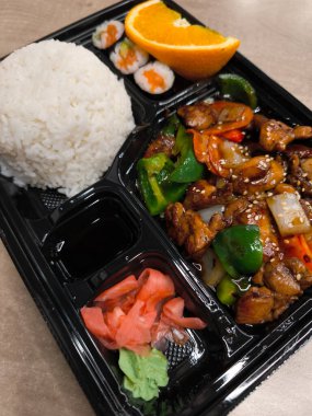 Teriyaki tavuğu, pilav, suşi, portakal dilimleri, zencefil, wasabi ve soya sosu içeren Bento kutusu, çeşitli ve lezzetli bir fast food sunuyor.