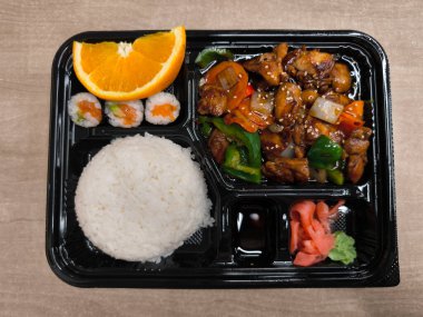 İçinde sebze, pirinç, suşi, turşu, zencefil, wasabi, soya sosu ve bir dilim portakallı fast food bulunan teriyaki tavuğunun genel manzarası.