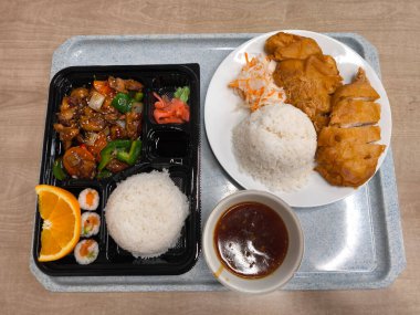 Asya yemek tepsisinde pilav, tavuk, suşi ve soslu fast food gibi çeşitli yemekler sunuluyor.