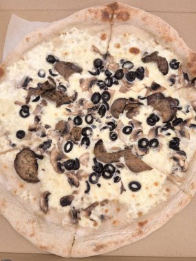 Mantarlı ve siyah zeytinli taze bir pizzanın üst görüntüsü, karton bir kutuda servis ediliyor, iştah açıcı sunumunu sunuyor.
