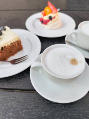 Kremalı kapuçino, havuçlu pasta ve kremalı tatlı Prag, Czechia 'da koyu ahşap bir masada servis edilerek nefis bir kafe sahnesi yaratıldı.