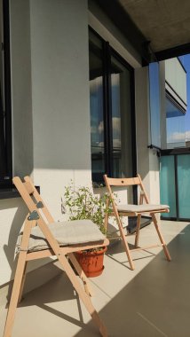 İki ahşap katlanır sandalye Prag, Czechia 'da güneşli bir balkonda oturur, bir saksı bitkisi ile dinlenmek için huzurlu bir yer sunar.