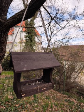 Ağaçtan sarkan tahta kuş besleyicisi Prag 'daki bir bahçede tohum ile birlikte bulutlu bir bahar günü,