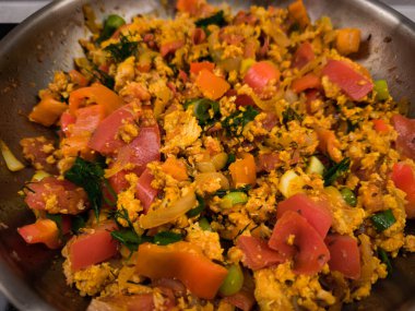 Gri bir mutfak yüzeyinde kızgın bir tavada canlı sebze ve otlarla karıştırılmış yer tavuğu.