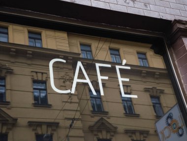 Prag, Çek Cumhuriyeti - 15 Nisan 2025: Cam bir pencereye yerleştirilmiş beyaz kafe tabelası, zarif bir toprak bina cephesini yansıtıyor ve sokak manzarasına cazibe katıyor