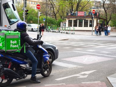 Prag, Çek Cumhuriyeti - 15 Nisan 2025: İzotermal sırt çantalı yiyecek dağıtıcısı motosiklet sürüyor ve Avrupa 'nın bir şehrinde trafik ışıklarında bekliyor