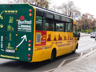 Prag, Çek Cumhuriyeti - 15 Nisan 2025: Pilsner Urquell markalı sarı otobüs Prag şehri turlarını tanıtıyor, kolay rezervasyon için bir soru kodu sunuyor
