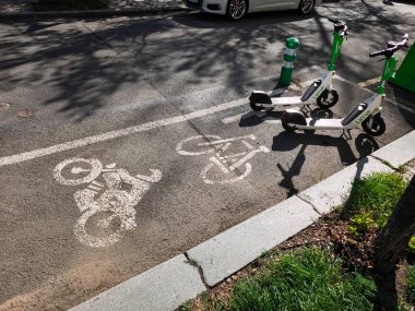 Prag, Çek Cumhuriyeti - 16 Nisan 2025: Sürdürülebilir kentsel ulaşımı temsil eden asfalt yolda bisiklet şeridi sembolünün yakınına park edilmiş iki elektrikli scooter