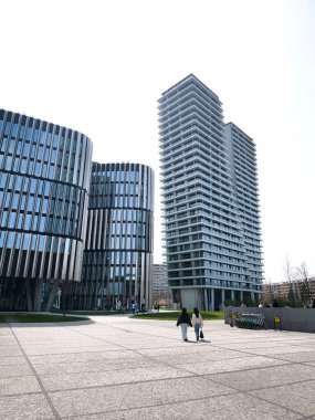 Prag, Çek Cumhuriyeti - 12 Nisan 2025: Çağdaş mimari ile modern bir iş bölgesinde yürüyen iki kadın Prag 'ın na strzi bölgesinin canlı kentsel manzarasını sergiliyor