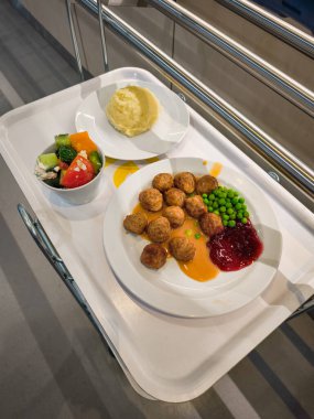 Prag, Çek Cumhuriyeti - 12 Nisan 2025: Beyaz ikea tepsisinde patates püresi, salata, sos, yaban mersini sosu ve bezelye ile servis edilen lezzetli İsveç köfteleri