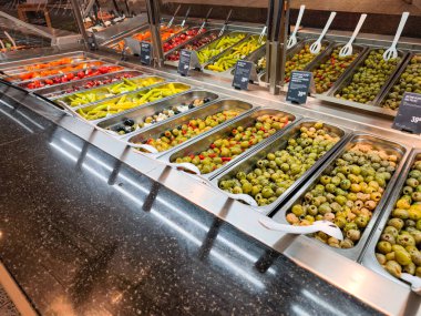 Prag, Çek Cumhuriyeti - 12 Nisan 2025: Çeşitli zeytin, biber ve diğer antipastilerin bulunduğu metal tepsiler, müşterilerin seçmeleri için Hypermarket globusunda bir şarküteri tezgahında düzenlenmiştir.