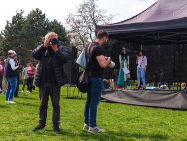 Prag, Çek Cumhuriyeti - 12 Nisan 2025: Prag parkında nauryz şenlikleri sırasında iki fotoğrafçı geleneksel giyinmiş kadınları sahnede yakaladı