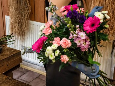 Çiçekçi eldiven takıyor. Renkli bir buket çiçek düzenliyor. Göz kamaştırıcı bir çiçek aranjmanı oluşturuyor.