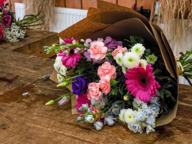 Kahverengi kağıda sarılı çeşitli çiçeklerden oluşan renkli buket bir çiçekçinin tezgahında yatıyor.