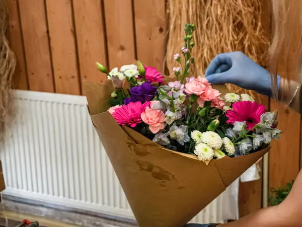 Çiçekçi dükkanında çeşitli çiçeklerden oluşan renkli bir buket hazırlayan, teslimat ya da müşteri almaya hazırlanan eldivenler giyen bir çiçekçi.