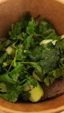 Taze kişniş, doğranmış yeşil soğan ve ahşap bir kaseye yerleştirilmiş baharatlar.