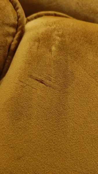 Yıpranmış ve yıpranmış hardal sarısı kadife döşeme, hasarı vurguluyor ve kanepe kullanımından aşınıyor.