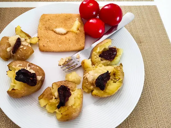 Beyaz bir tabağa yerleştirilmiş, üzerinde koyu renkli malzemeler, parlak kırmızı kiraz domatesleri ve tatlı bir tatlıyla birlikte, davetkar bir yemek takımı oluşturan, altın-kahverengi fırınlanmış patates.