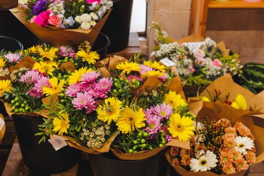 Kasımpatı, papatya ve diğer türler gibi renkli çiçek buketleri kahverengi kağıda sarılır ve satılmaya hazır siyah kovalara konur.