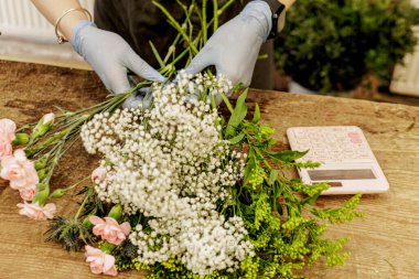Çiçekçi eldiven takıyor, çigila, karanfil ve soya çiçeğini hesap makinesiyle ahşap bir masada düzenliyor. Anneler Günü.