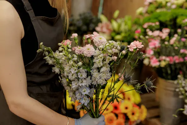 Çiçekçi dikkatlice bir buket rengarenk tarla kuşu, karanfil ve eryngium yerleştirirken çiçekçi dükkanında çeşitli çiçek kovanlarıyla çevrili Anneler Günü