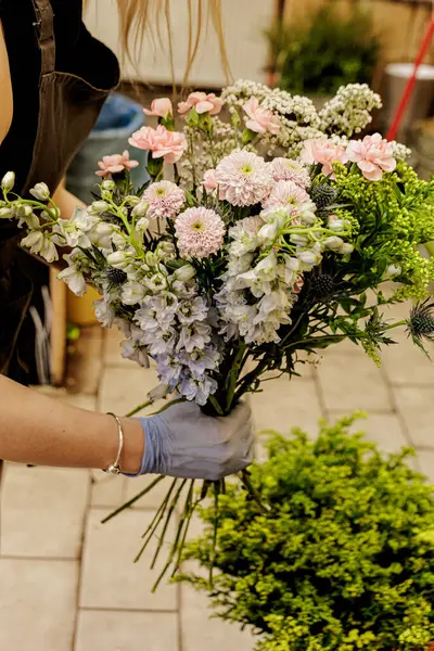 Çiçekçi ustalıkla eldivenler giyer büyüleyici bir çiçekçide canlı bir buket pembe ve mavi çiçek düzenler, çiçek sanatını gözler önüne serer, Anneler Günü