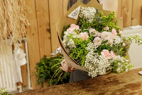 Çiçekçi, kırsal bir çiçekçide kahverengi kağıda sarılı güzel bir buket taze çiçek hazırlıyor. Anneler Günü.