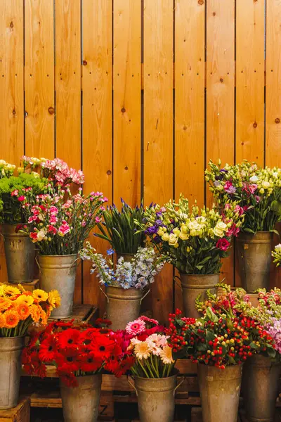 Metal kovalara yerleştirilmiş canlı çiçek buketleri ahşap sandıkların üzerinde kırsal ahşap bir duvara karşı oturur ve büyüleyici bir çiçek dekoru oluşturur.