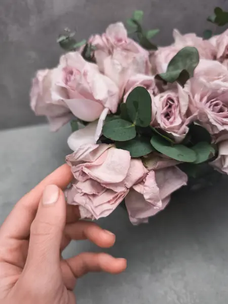 Çiçekçi, gelin buketinde pembe bir gülü nazikçe okşayarak arka plandaki duvar kâğıdına bir zarafet katıyor.