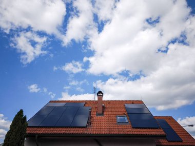 Açık mavi gökyüzü altında, yenilenebilir enerji ve sürdürülebilirliğin önemini vurgulayan, kabarık bulutlarla dolu modern çatı.