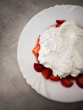 Taze çilekler tabağa dizilmiş, bol bol krema ile kaplanmış, her durum için mükemmel bir tatlı yaratıyor, canlı renkler ve dokular sergiliyor. Boşluğu kopyala