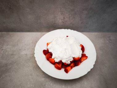 Beyaz bir tabağa konmuş taze çilekler, bol bol köpüklü kremayla kaplanmış, canlı renkleri ve dokuları vurgulayan çekici bir tatlı sunumu yaratıyor. Boşluğu kopyala