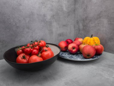 Basit bir gri arka plan duvar kağıdı fotokopi alanına karşı dizilmiş taze domatesler ve elmalar sergileniyor.