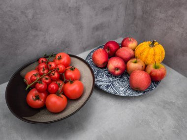 Domates, elma ve süs kabağı tabakları gri bir yüzeye oturup, arka planda yeni üretilen duvar kağıdı kopyalama alanı sunar.