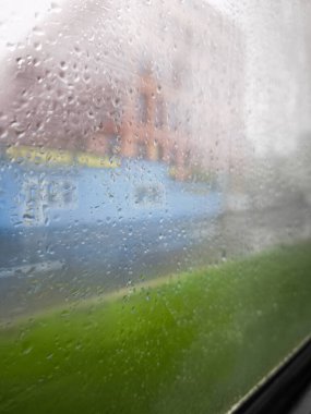 Damlacıklarla dolu yağmurlu pencere manzarası dışarıdaki manzarayı bulanıklaştırıyor, sakin ve sakin bir atmosferde kentsel yaşamı ve doğa unsurlarını vurguluyor