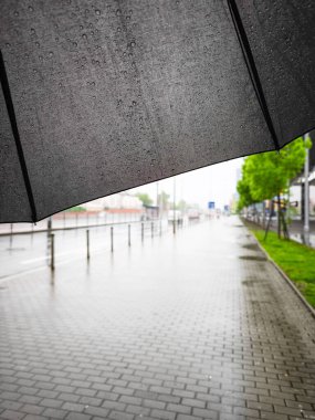 Yağmurlu bir günde yağmurlu bir şemsiyeyle ıslak bir kaldırımda yağmurdan korunan şehir manzarasını ve doğanın güzelliğini vurgulayan bir sahne.
