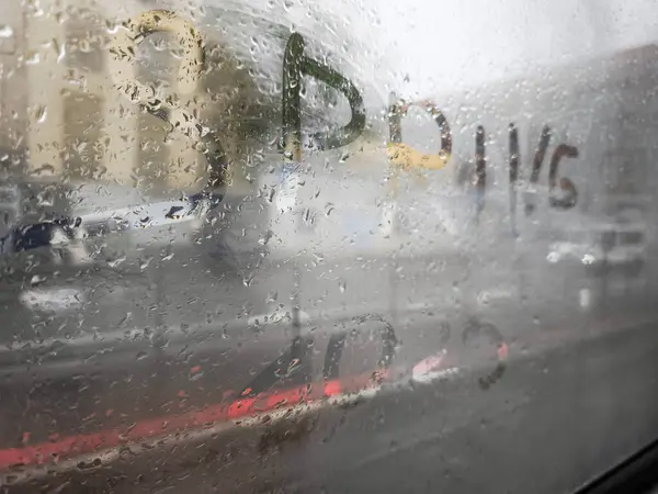 Parlak yazılar ile süslenmiş yağmurlu bir pencere, dış görünüşü bulanık bir perspektif sunuyor. Nostalji ve bahar zamanı yansımalarını yansıtıyor.